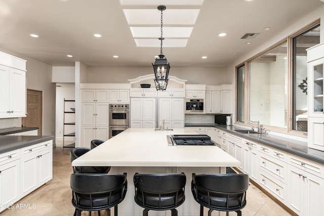 kitchen featuring appliances with stainless steel finishes, a breakfast bar, sink, decorative light fixtures, and a center island with sink