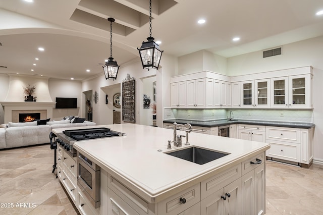 kitchen with a kitchen island with sink, sink, a fireplace, decorative light fixtures, and white cabinetry