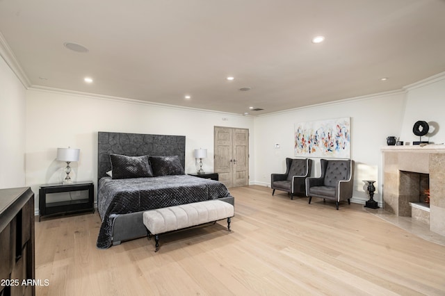 bedroom featuring a tile fireplace, crown molding, and light hardwood / wood-style floors