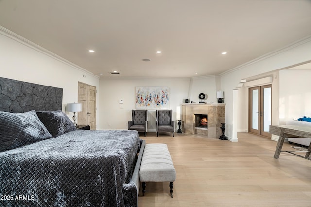 bedroom with crown molding, a large fireplace, light hardwood / wood-style floors, and french doors