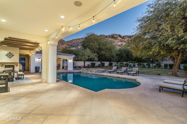 pool at dusk with a patio area, a mountain view, and exterior fireplace