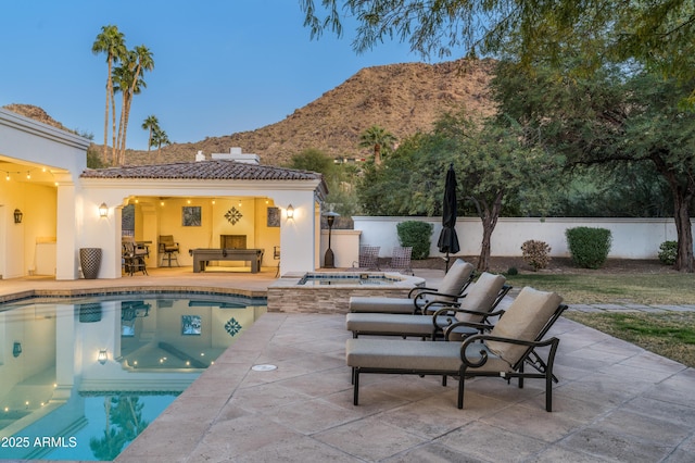 pool at dusk with a mountain view, a patio, and an in ground hot tub