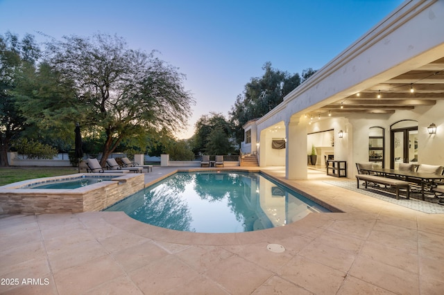 pool at dusk featuring an in ground hot tub and a patio