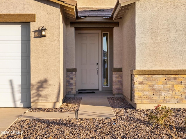 entrance to property with a garage, stone siding, and stucco siding