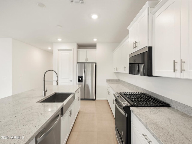 kitchen featuring recessed lighting, appliances with stainless steel finishes, white cabinetry, a sink, and light stone countertops