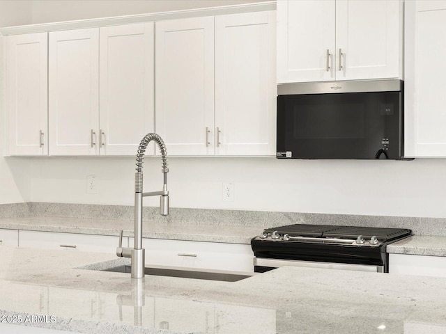 kitchen featuring light stone counters, white cabinets, and gas range