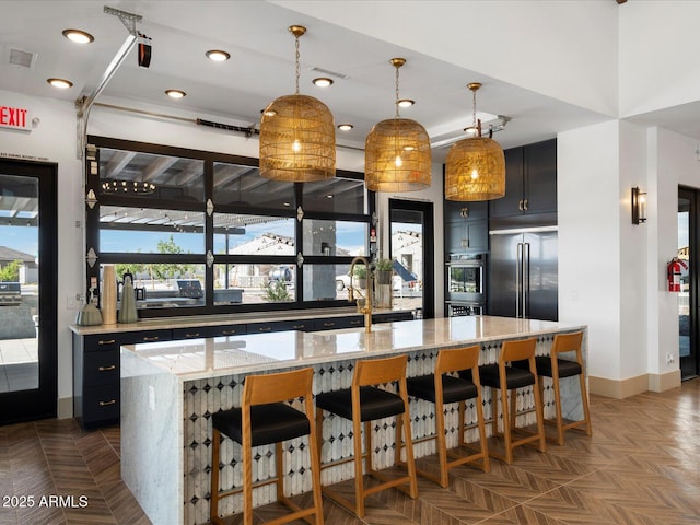 kitchen featuring light stone counters, a center island, hanging light fixtures, dark cabinets, and a kitchen bar