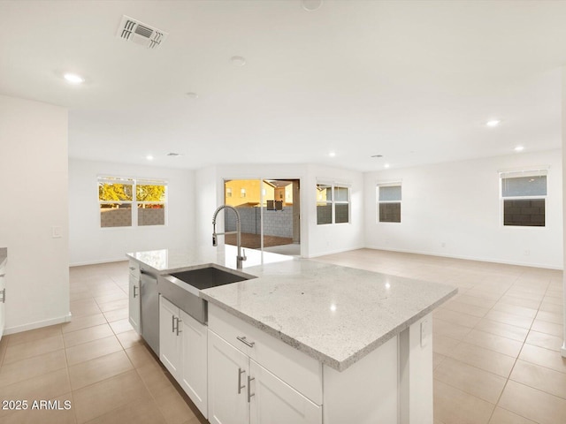 kitchen with visible vents, an island with sink, light stone counters, white cabinetry, and a sink