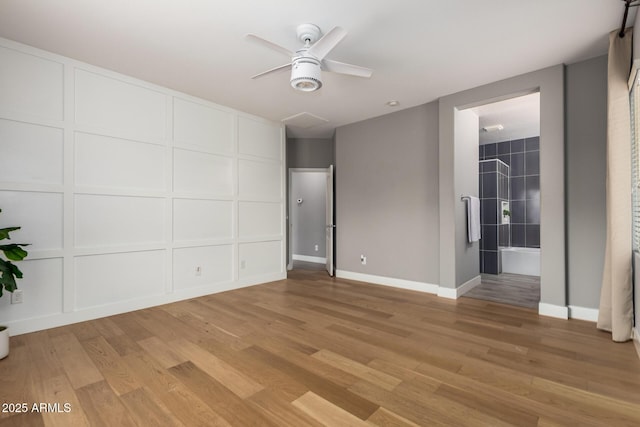 empty room featuring light wood-style flooring, a decorative wall, a ceiling fan, and baseboards