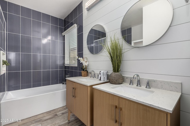 bathroom featuring two vanities, wood finished floors, tub / shower combination, and a sink