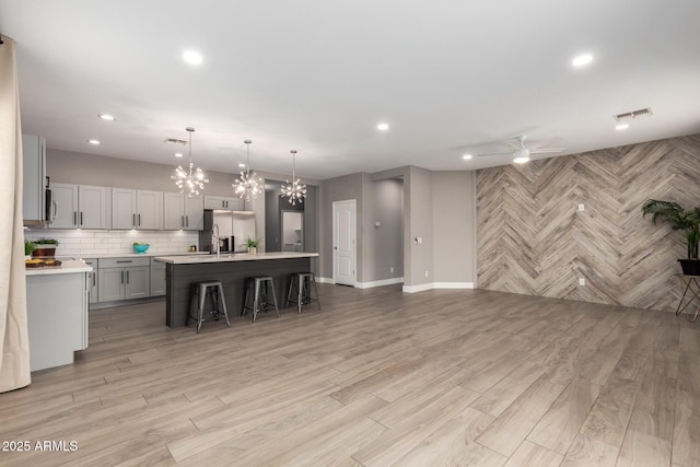 kitchen featuring visible vents, backsplash, light countertops, ceiling fan with notable chandelier, and stainless steel fridge