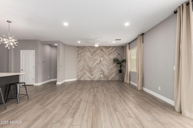 unfurnished living room featuring visible vents, light wood-style flooring, ceiling fan with notable chandelier, recessed lighting, and an accent wall