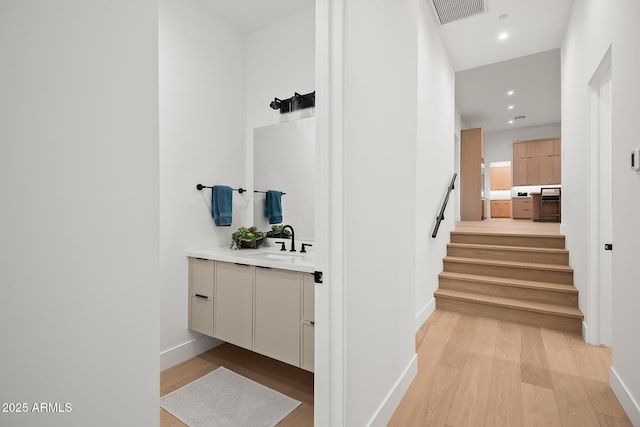 hall featuring visible vents, light wood-style floors, baseboards, and a sink