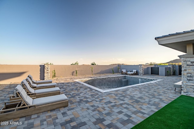 pool at dusk with a patio, a fenced backyard, and a fenced in pool