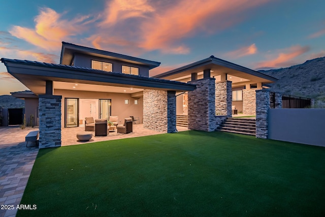 back of house with a patio, a yard, stone siding, an outdoor hangout area, and stucco siding