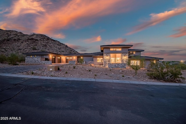 prairie-style home with driveway, stone siding, a mountain view, stucco siding, and a garage