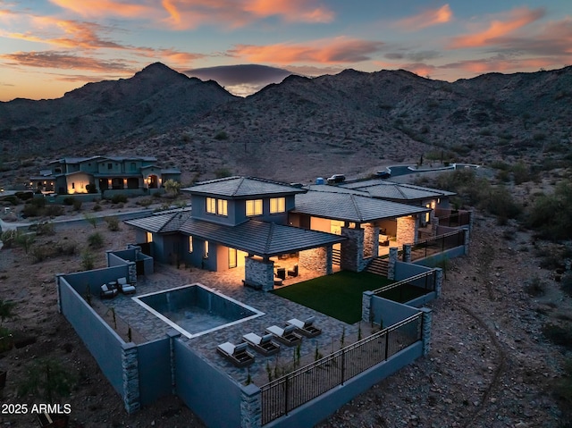 back of property with a mountain view, a fenced backyard, stucco siding, and stone siding