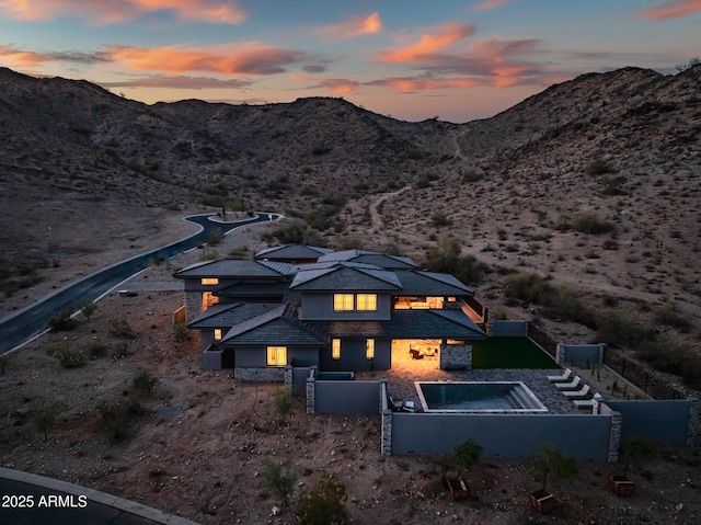 back of house at dusk featuring a fenced in pool, a mountain view, a desert view, and a fenced backyard