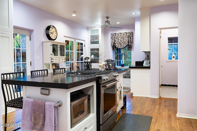 kitchen featuring stainless steel appliances, a kitchen bar, white cabinets, light hardwood / wood-style floors, and ceiling fan