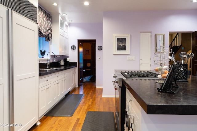 kitchen featuring white cabinetry, stainless steel range with gas cooktop, light hardwood / wood-style flooring, and sink