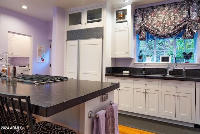 kitchen with paneled built in fridge, sink, white cabinetry, and light wood-type flooring