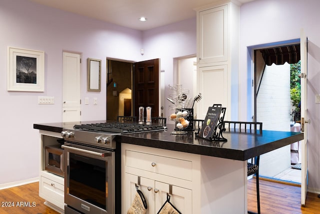 kitchen with white cabinets, a kitchen bar, light hardwood / wood-style flooring, and high end stainless steel range oven