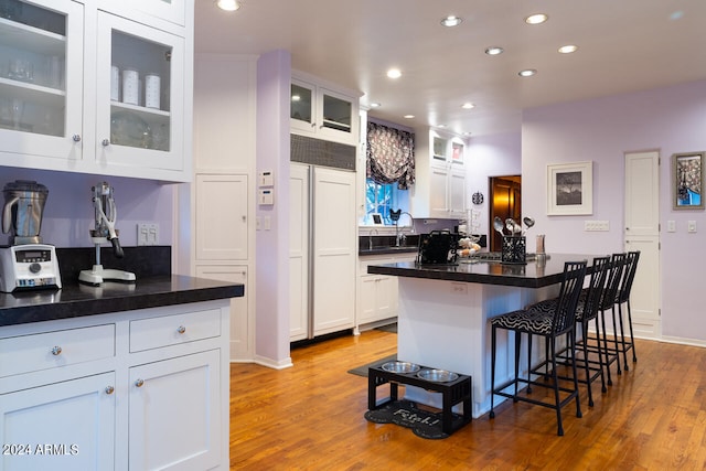 kitchen with a kitchen breakfast bar, light hardwood / wood-style flooring, sink, a center island, and white cabinetry