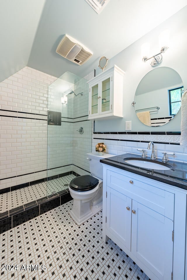 bathroom featuring tiled shower, toilet, tile patterned flooring, vanity, and tile walls