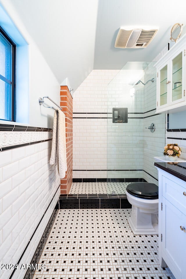 bathroom with tiled shower, toilet, vanity, vaulted ceiling, and tile walls