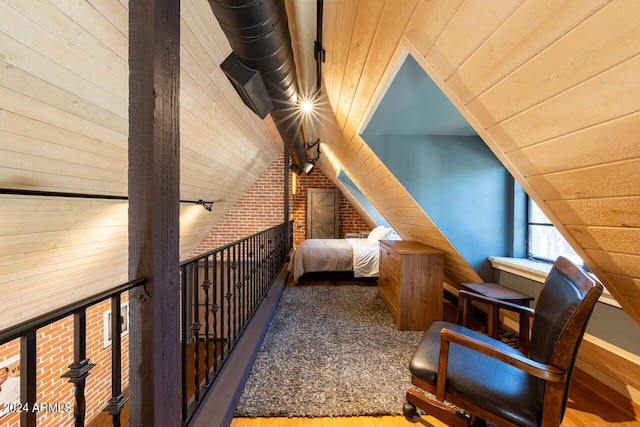 interior space with brick wall, wood-type flooring, lofted ceiling, and wooden walls