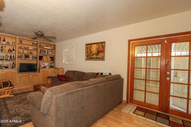 living area featuring a ceiling fan, french doors, a textured ceiling, and light wood finished floors