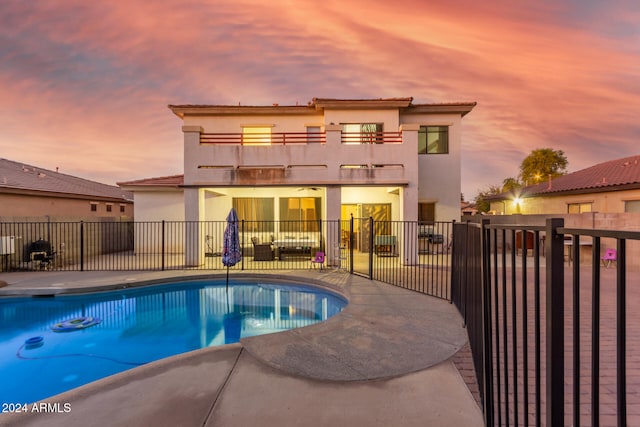 back house at dusk with a fenced in pool and a balcony