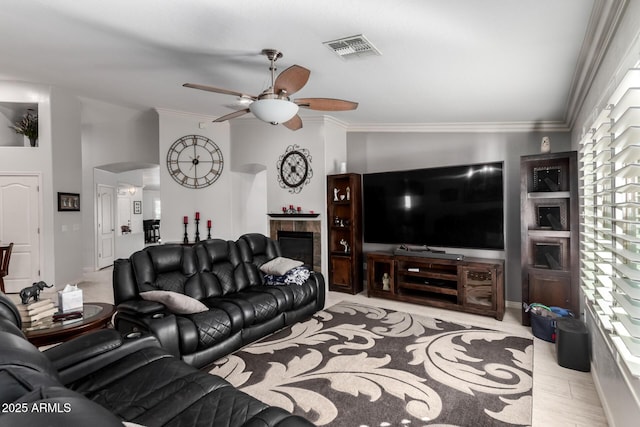 living room featuring ceiling fan, crown molding, and a tiled fireplace