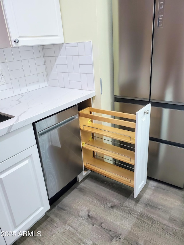 kitchen with hardwood / wood-style floors, white cabinets, stainless steel appliances, decorative backsplash, and light stone counters