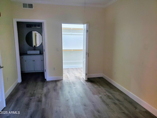 interior space featuring a walk in closet, connected bathroom, crown molding, and dark wood-type flooring