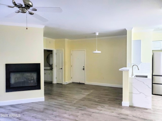 unfurnished living room featuring sink, ceiling fan, crown molding, and light hardwood / wood-style floors