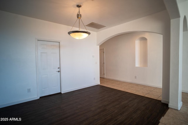 unfurnished room with wood finished floors, baseboards, visible vents, and arched walkways