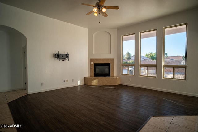 unfurnished living room featuring a fireplace, ceiling fan, baseboards, arched walkways, and wood finished floors