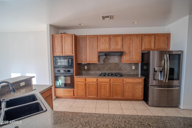 kitchen with a sink, brown cabinetry, black appliances, visible vents, and backsplash
