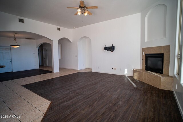unfurnished living room featuring visible vents, baseboards, a tile fireplace, wood finished floors, and a ceiling fan