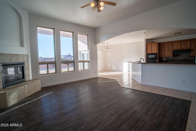 unfurnished living room with a sink, visible vents, a fireplace, wood finished floors, and a ceiling fan