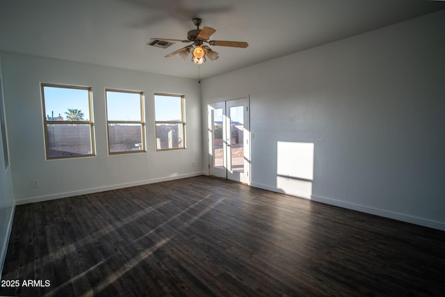empty room with dark wood-type flooring, visible vents, a ceiling fan, and baseboards