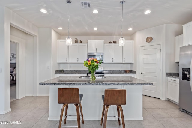 kitchen with visible vents, a breakfast bar, an island with sink, appliances with stainless steel finishes, and light tile patterned flooring