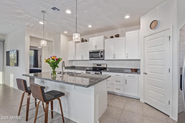 kitchen with visible vents, a kitchen island with sink, a sink, white cabinetry, and stainless steel appliances