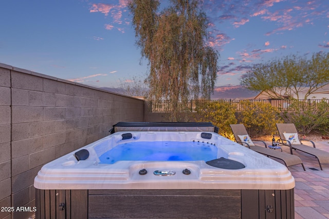 patio terrace at dusk featuring a fenced backyard and a hot tub