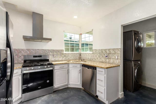 kitchen featuring wall chimney exhaust hood, sink, white cabinetry, appliances with stainless steel finishes, and stacked washing maching and dryer