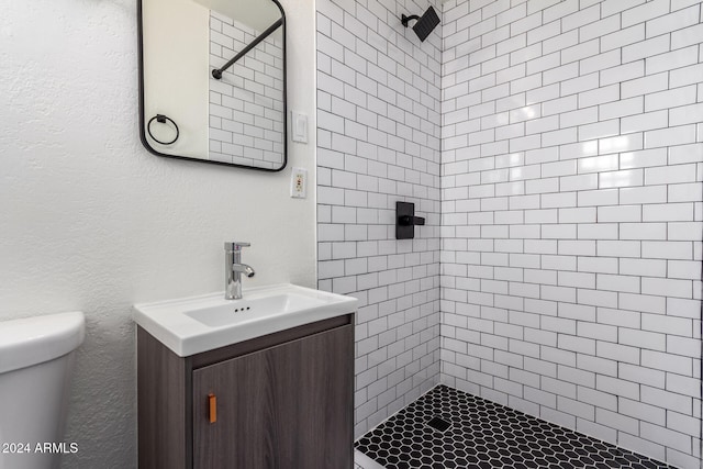 bathroom featuring vanity, a tile shower, and toilet