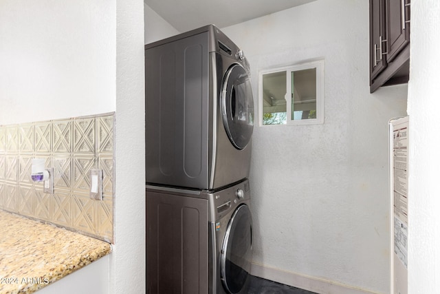 clothes washing area featuring cabinets and stacked washing maching and dryer