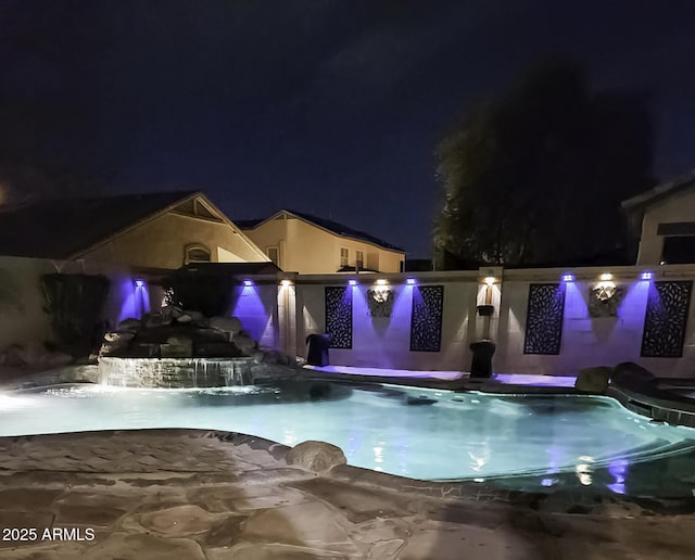 pool at night with a fenced in pool and a jacuzzi
