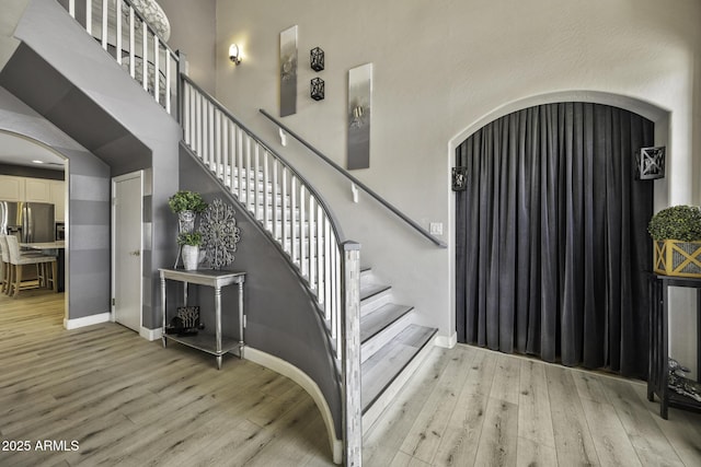 stairway with baseboards, arched walkways, and wood finished floors